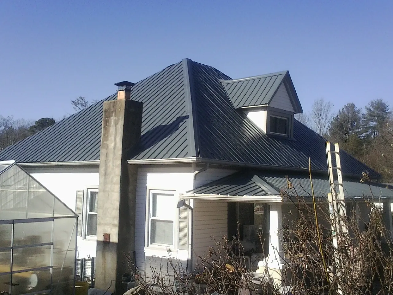 Dark blue standing seam metal roof on a white farmhouse with dormer — Slate & Tile Roof Repair by Roofing Brothers in Bee