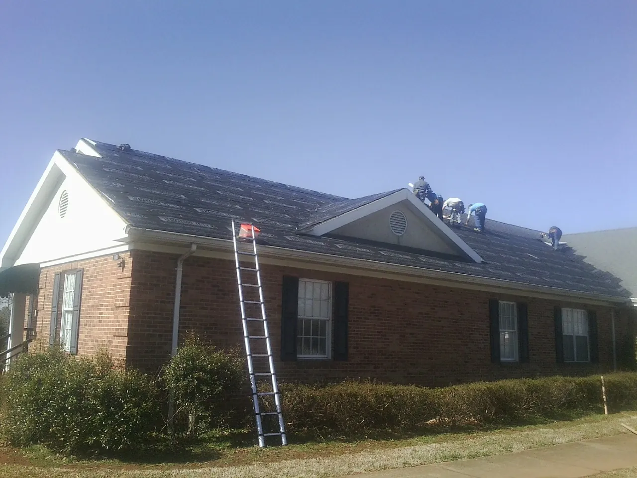 Crew tearing shingles off a brick ranch roof with a ladder set — Metal Roof Repair work by our crew in Bee