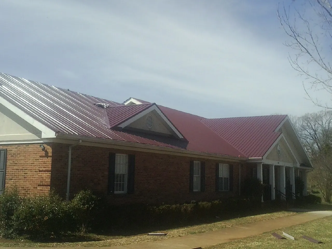 Red metal roof with gabled entries on a long brick building, from a Hail Damage Roof Repair job in Bee