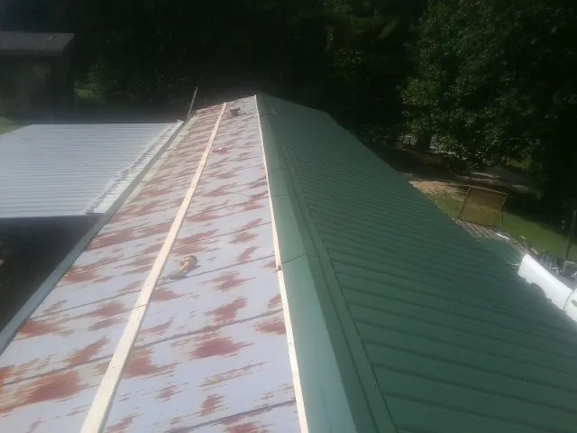 Old rusted panels beside newly installed green metal roofing — Wind Damage Roof Repair by Roofing Brothers in Bee