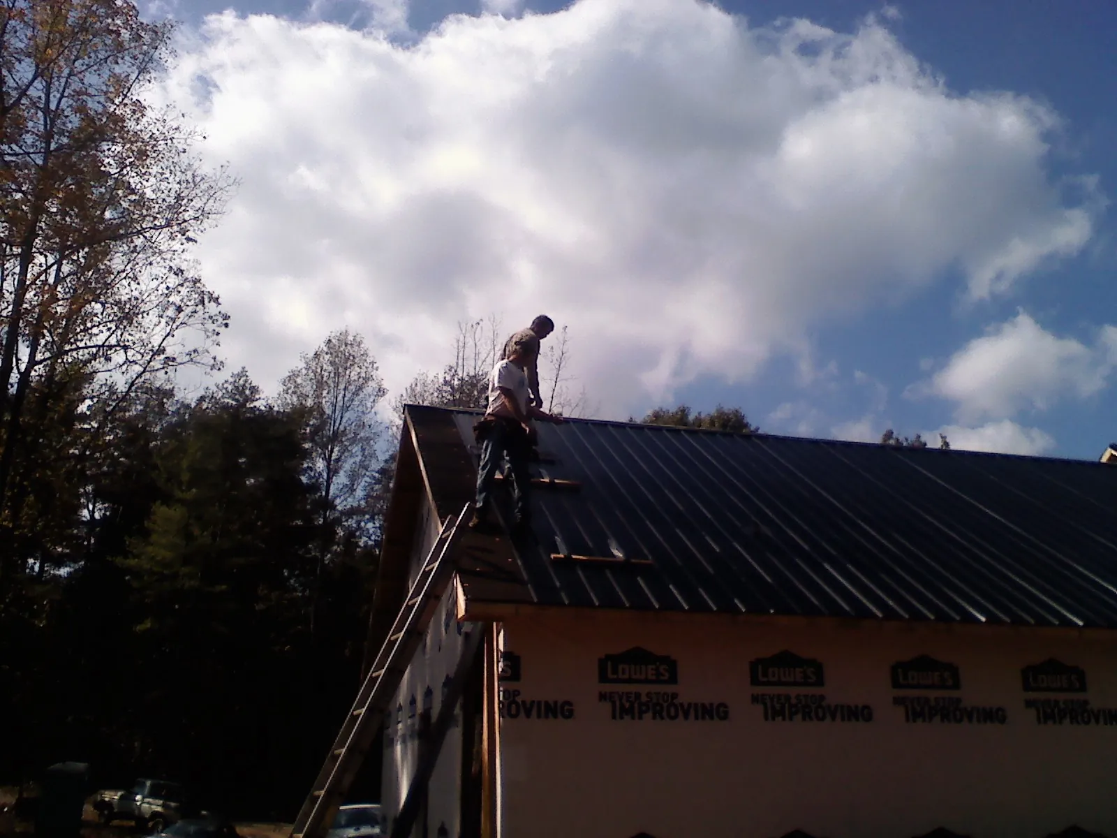 Roofer fastening dark metal panels high against a cloudy sky, from a Roof Inspection job in Bee