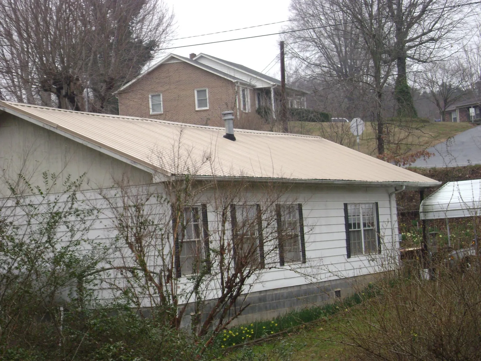 Tan metal roof on a white sided house set into a hillside — Commercial Roofing by Roofing Brothers in Bee