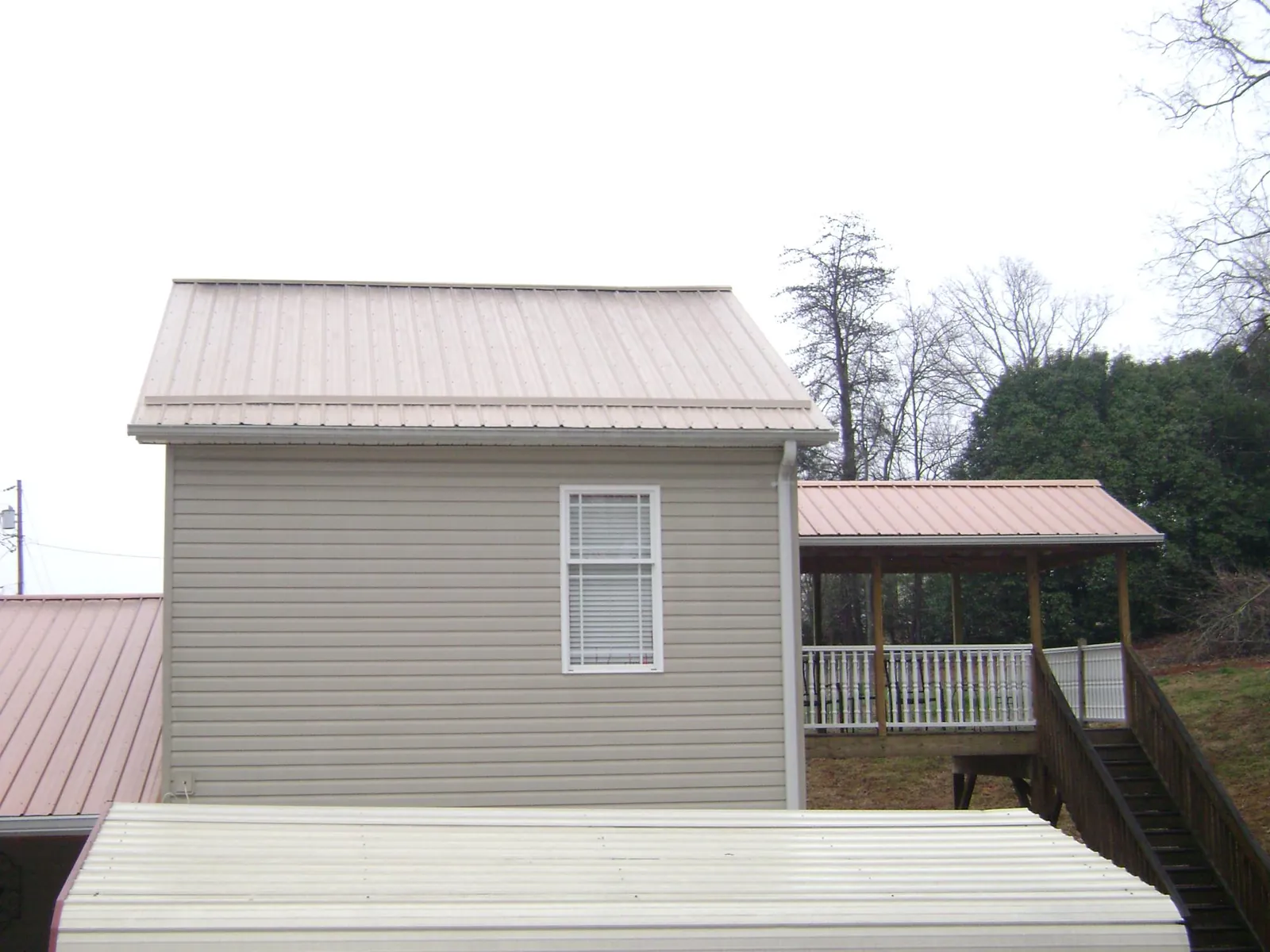 Tan metal roofs on a two story addition and attached porch, from a Roof Replacement job in Bee